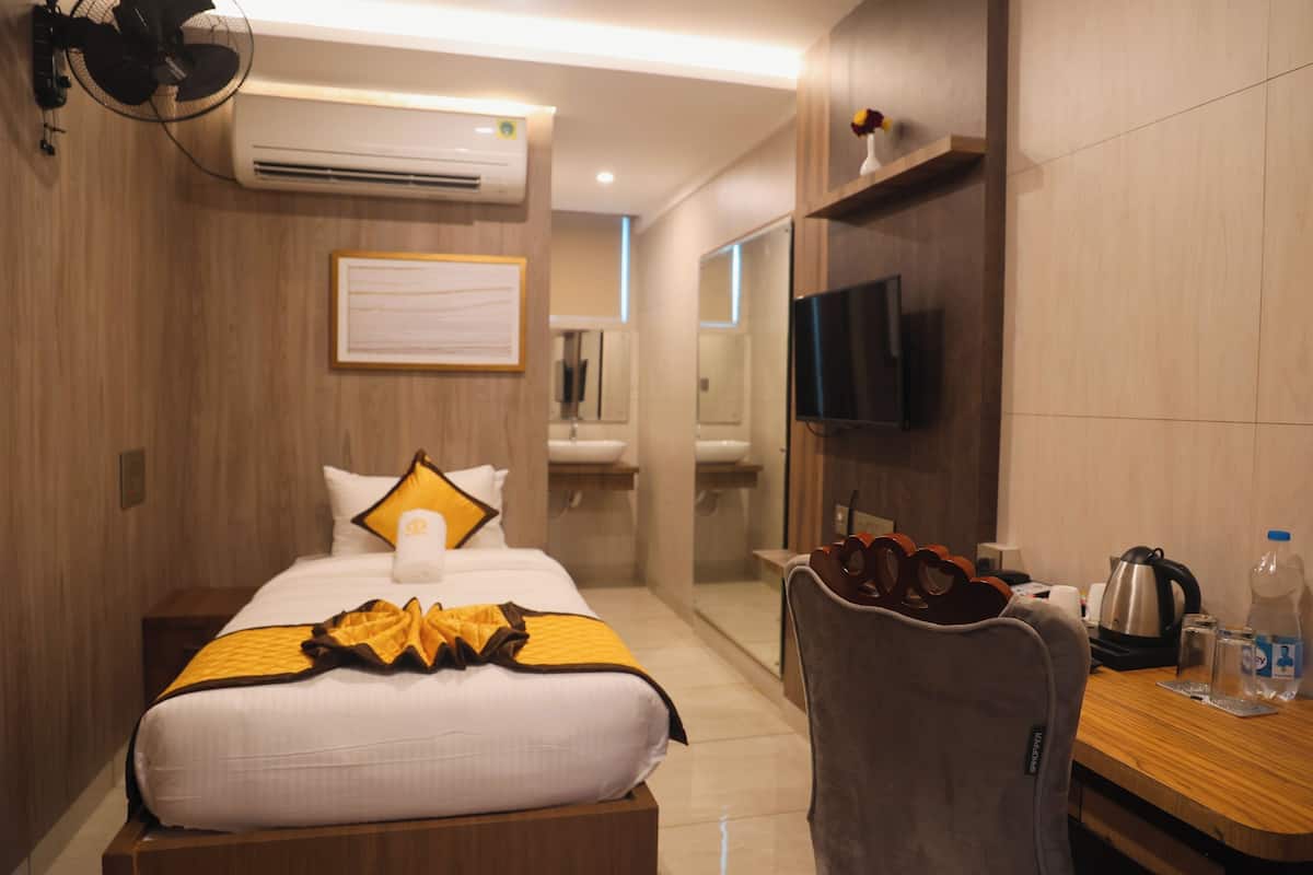 A hotel room with a bed, a desk with a kettle, a chair, and a TV on the wall.