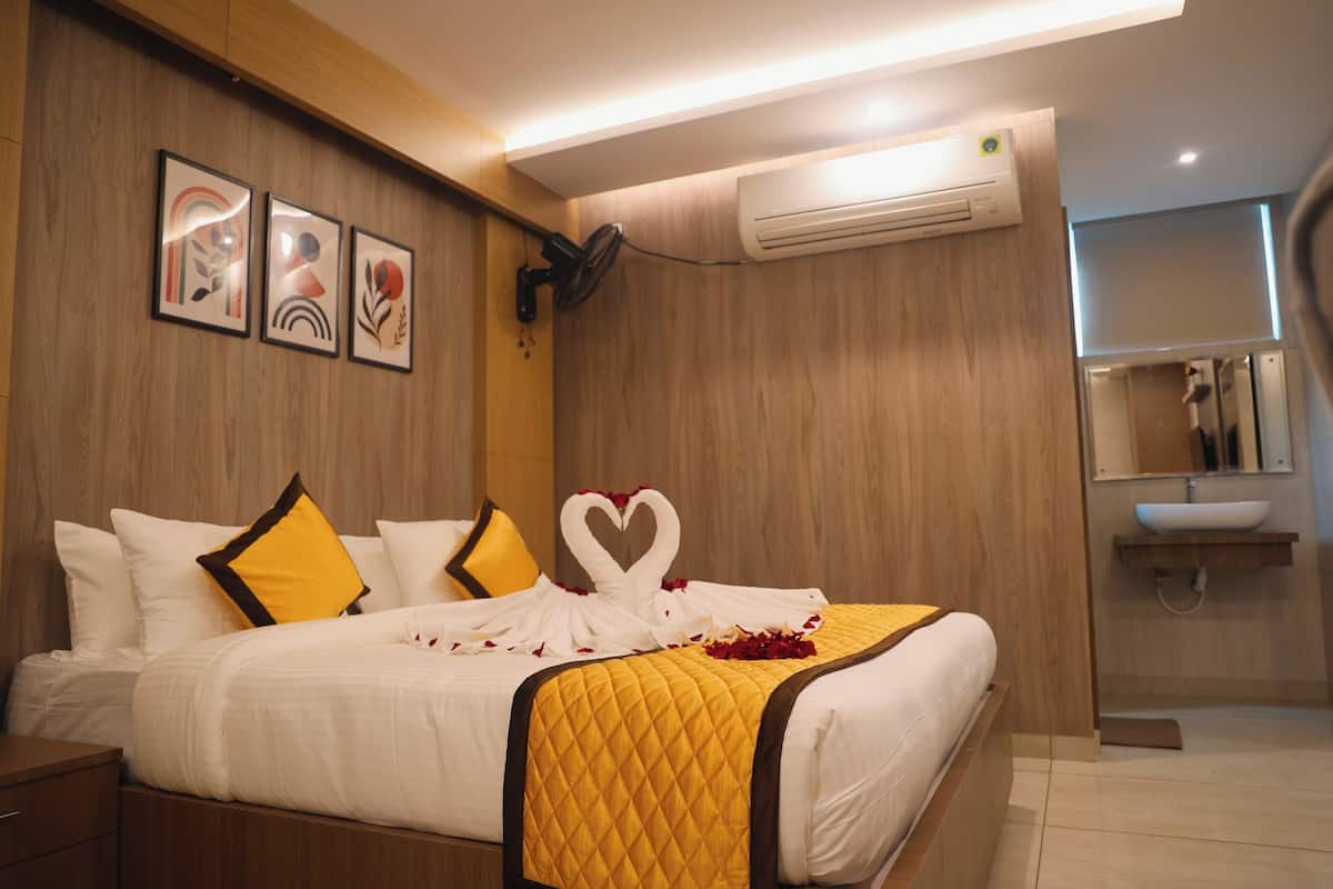 A hotel room with a bed, a bedside table, a wall-mounted air conditioner, and a bathroom with a sink and mirror.