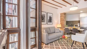 A modern living room with a grey sofa, a glass coffee table, and a dining area with a white table and chairs. - Luxury Suite Dar Garnata (Granada)