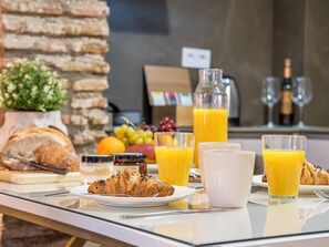 Une table dressée pour le petit-déjeuner, avec des croissants, des fruits et du jus d’orange.