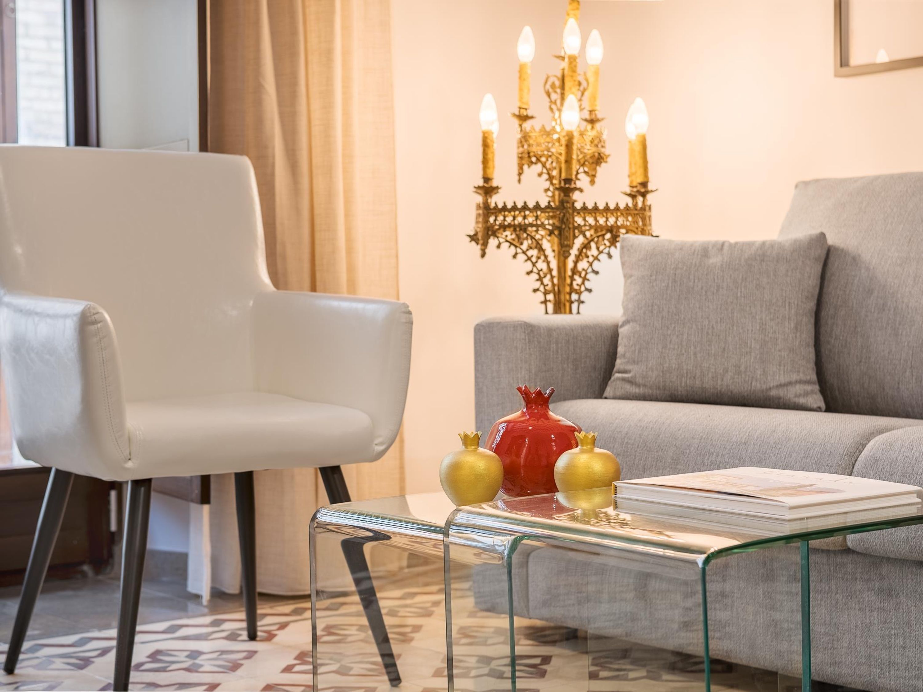 Una sala de estar moderna con una silla blanca, un sofá gris, una mesa de centro de cristal con adornos y una araña.