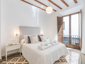 Une chambre avec un grand lit, une table de chevet, une tête de lit décorée et une vue sur le balcon extérieur.