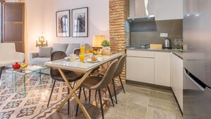 A modern kitchen with a brick accent wall, a dining area with a glass table, and a cozy seating area with a sofa and a chandelier. - Luxury Suite Dar Garnata (Granada)