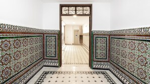 Un couloir aux murs et au sol ornés de motifs complexes en mosaïque, qui mène à une porte au fond.