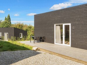 A modern building with a dark exterior, a wooden deck, and a glass door entrance. - Great Cabin in Camping Resort (Aabenraa)