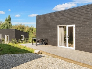 A modern building with a dark exterior, a wooden deck, and a glass door entrance. - Great Cabin in Camping Resort (Aabenraa)