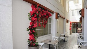 A café with white chairs and tables, a large potted plant with red flowers, and a patterned floor. - PRUVA INN HOTEL (Antalya)
