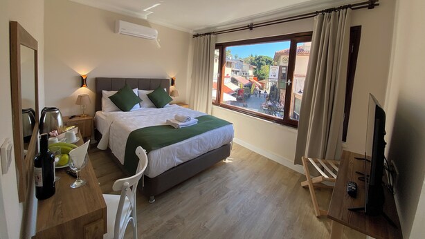A hotel room with a bed, bedside table, lamp, TV, and a window with a view of the street. - PRUVA INN HOTEL (Antalya)