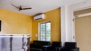 A room with yellow textured walls, a ceiling fan, an air conditioning unit, a window with bars, and three black chairs.