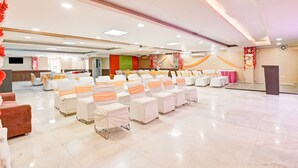 Een ruime zaal met rijen stoelen bekleed met wit en oranje, een podium en een buffettafel.