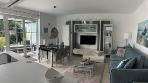 A modern living room with a grey sofa, a dining table, and a TV. - Modern vacation apartment with view and pool near Baden Baden in the Black Forest  (Gernsbach)