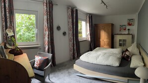 A bedroom with a bed, a wooden wardrobe, a desk with a lamp, and a window with curtains. - Modern vacation apartment with view and pool near Baden Baden in the Black Forest  (Gernsbach)