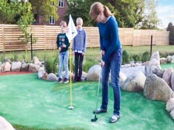 A person playing golf on a green field with rocks and a wooden fence in the background. - Pleasant Holiday Home Near the Beach (Aabenraa)