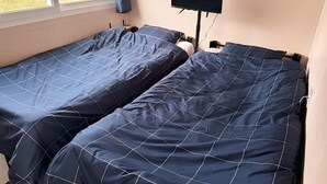 Zwei Einzelbetten mit blauer Bettwäsche, ein Flachbildfernseher an der Wand und ein Fenster mit Vorhängen.