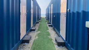 Eine Reihe blauer, mobiler Hütten mit einem grasbewachsen Weg zum Strand.
