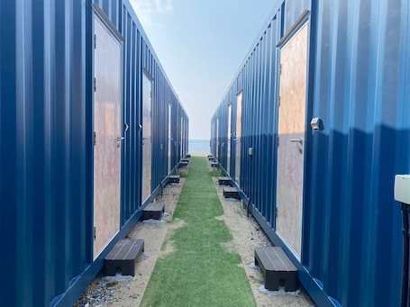 A row of blue portable cabins with a grassy path leading to the beach.