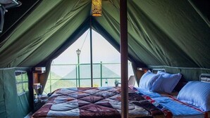 Een tent met een bed, een hanglamp en uitzicht op een groene omheining.