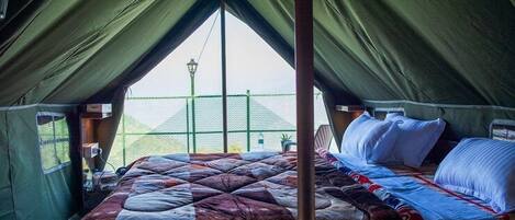 A tent with a bed, a hanging light, and a view of a green fence outside.