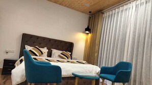 Een slaapkamer met een groot bed, twee blauwe stoelen, een klein tafeltje en een houten vloer.