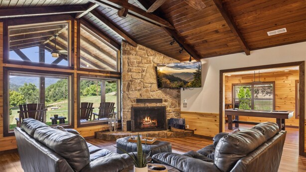 Una sala de estar acogedora con sofás de cuero, una chimenea de piedra y ventanas amplias con vistas al exterior.
