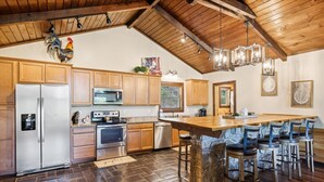 Una cocina amplia con armarios de madera, una isla grande con taburetes de bar, una pared de acento de piedra y un techo rústico.