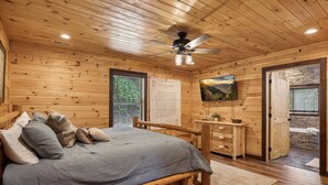 Un dormitorio tipo cabaña de madera con una cama, un aparador, un televisor y una pared de piedra.