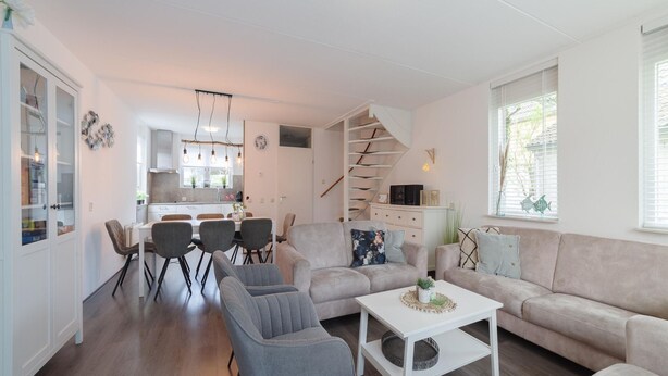 Ein modernes Wohnzimmer mit Sofa, Sesseln, einem Couchtisch und einer Treppe, die in den oberen Stock führt.