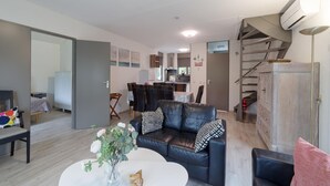 A modern living room with a sofa, coffee table, and a dining area in the background. - Holiday home: Bubbles, Bounce and Relax (Wemeldinge)