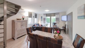 A dining area with a table set for four, a staircase, and a living area with a sofa and TV. - Holiday home: Bubbles, Bounce and Relax (Wemeldinge)