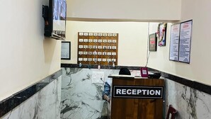Una zona de recepción con pared de mármol, mostrador de madera, televisor y tablón de anuncios.