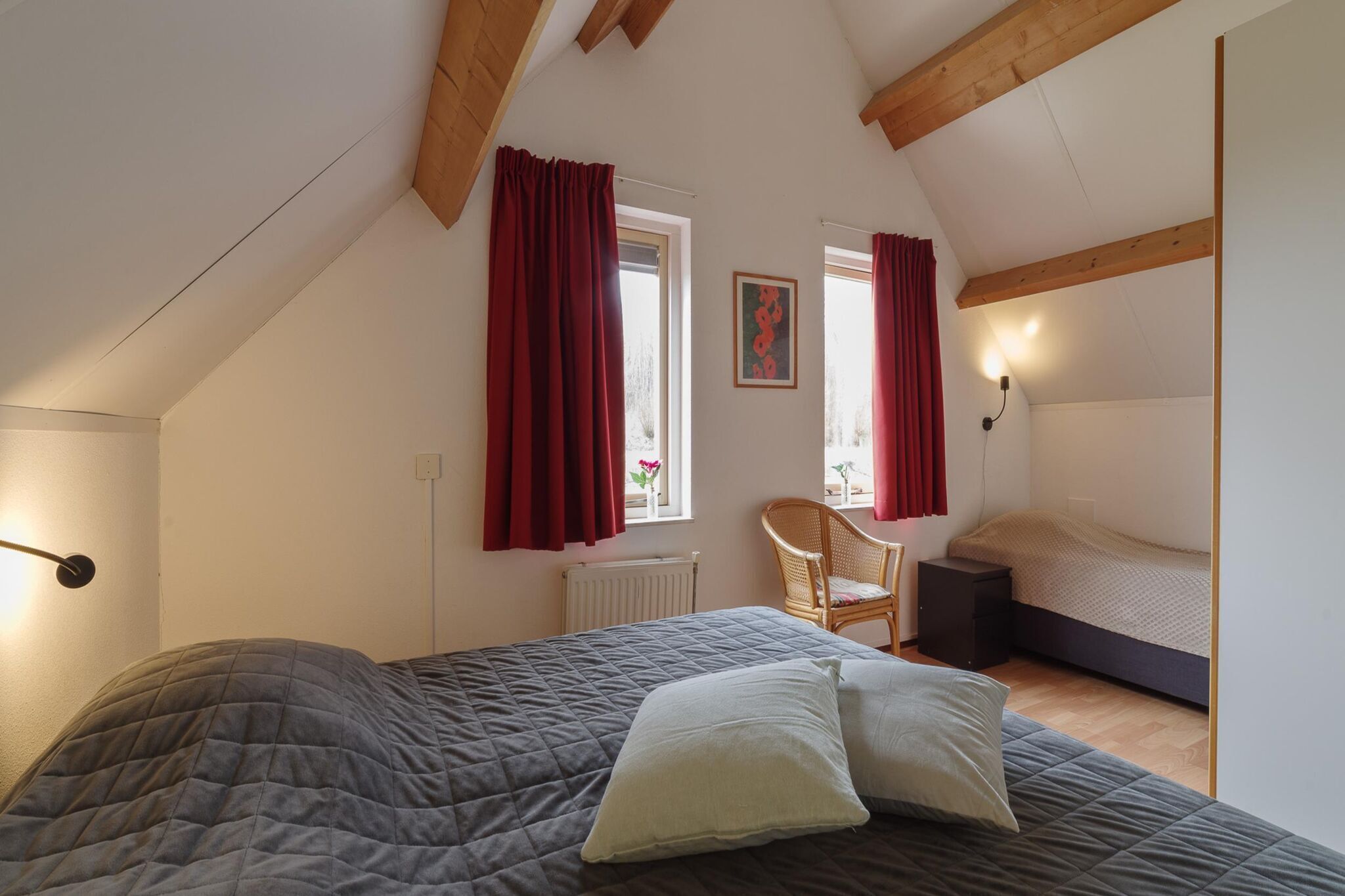 Een slaapkamer met een bed, een stoel, een radiator en een raam met gordijnen.