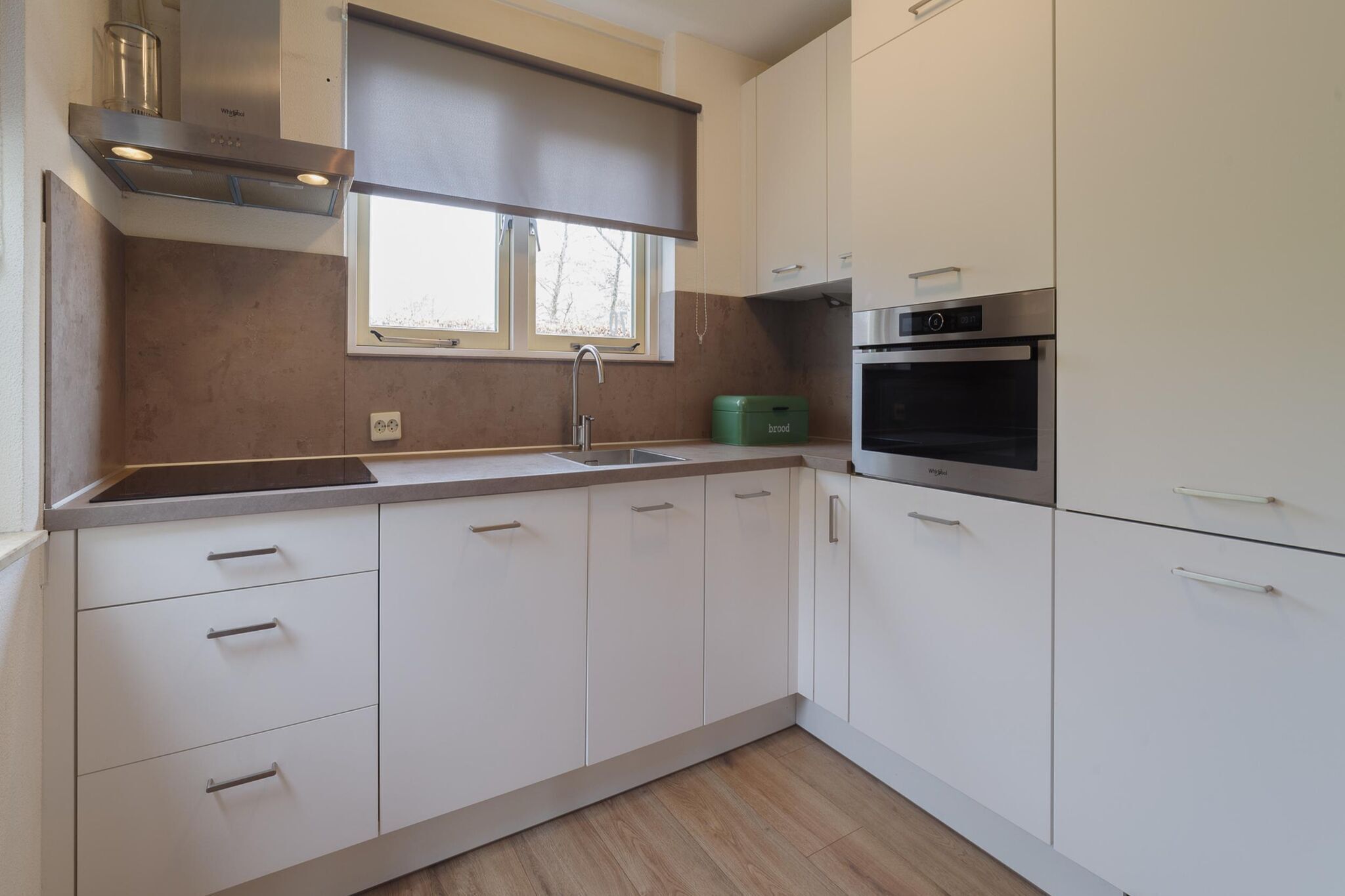 A modern kitchen with white cabinets, a stainless steel oven, and a window above the sink.