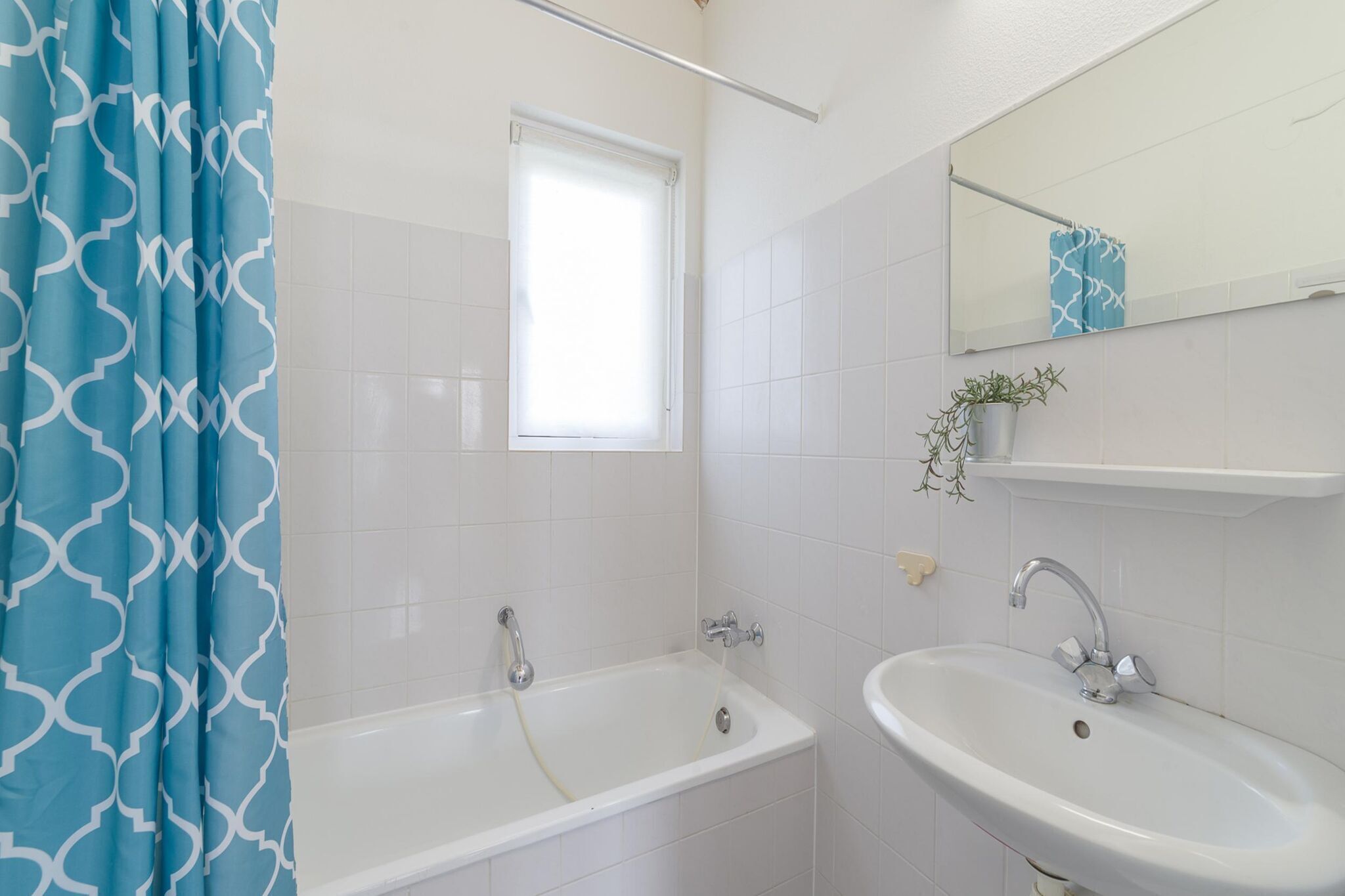 A bathroom with a bathtub, a sink, a window with a blind, and a mirror above the sink.