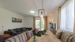 A modern living room with a sofa, a dining table, and a vase of flowers. - Holiday Home in Zeeland with Spacious Garden (Wemeldinge)