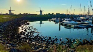 A marina with boats docked, a windmill in the background, and a calm water body reflecting the sky. - Spacious Coastal Getaway (Wemeldinge)