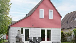 A red and white house with a chimney, a patio with chairs, and a brick wall.