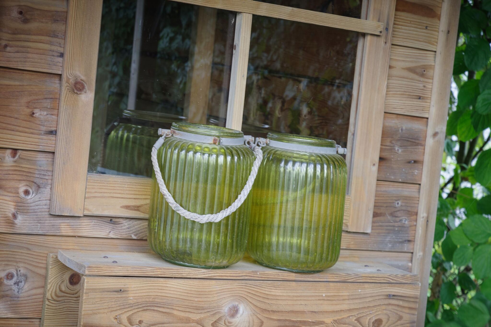 Deux bocaux en verre munis d’anses en corde, posés sur une étagère en bois.