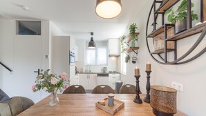 A dining area with a wooden table, chairs, a vase with flowers, a candle holder, and a wall-mounted shelf with plants. - Holiday Home in Quiet Park with Garden (Wemeldinge)
