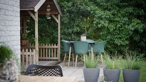 An outdoor patio with a wooden table and chairs, surrounded by potted plants and a wooden fence. - Holiday Home in Quiet Park with Garden (Wemeldinge)