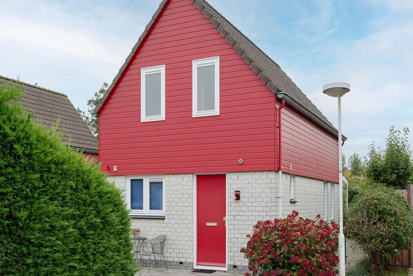 Una casa roja con puerta blanca, dos ventanas y un porche pequeño con sillas.