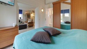 A bedroom with a bed, a dresser, a mirror, and a television on the wall. - Holiday Home in Zeeland with Garden Terrace (Wemeldinge)