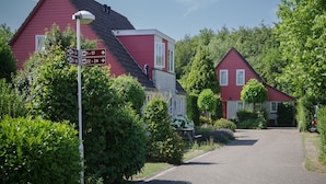 A red house with a sloped roof, surrounded by lush greenery and a clear sky. - Holiday Home in Zeeland with Garden Terrace (Wemeldinge)