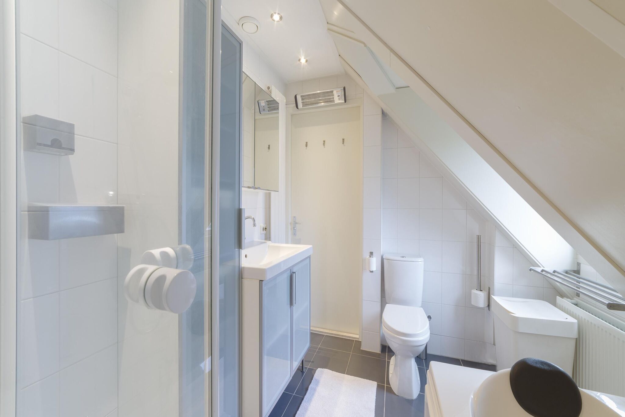 Un baño moderno con cabina de ducha de vidrio, un lavabo blanco y un inodoro.