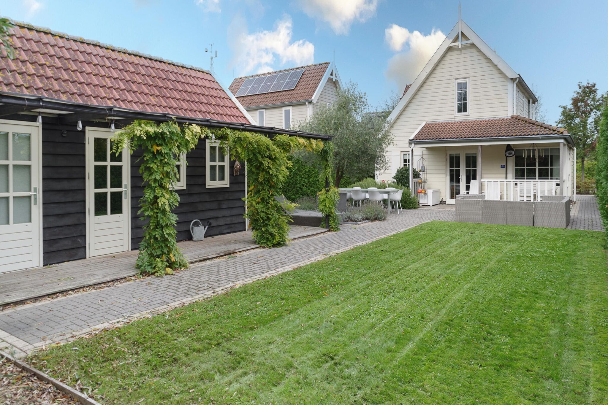 A residential area with a paved pathway leading to a house with a red-tiled roof and solar panels.