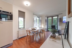 A modern kitchen with a built-in oven, a dining area with a white table and chairs, and a large window with curtains.