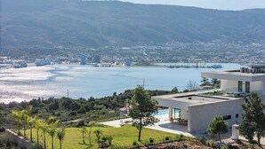 Ein modernes Haus mit Pool, mit Blick auf eine Küstenstadt und Berge.
