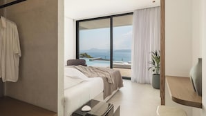 Ein modernes Schlafzimmer mit einem großen Bett, einem Nachttisch, Blick auf das Meer und einer Topfpflanze.