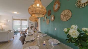 Een eethoek met een lange tafel gedekt voor een maaltijd, omringd door rieten lampen en geweven wanddecoraties.