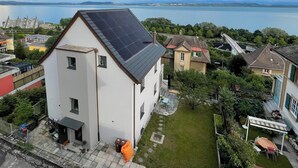 Een woongebouw met een dak voorzien van zonnepanelen, een kleine tuin en uitzicht op een meer.