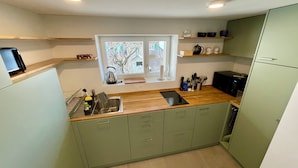 Een kleine keuken met raam, een houten aanrechtblad en groene keukenkastjes.
